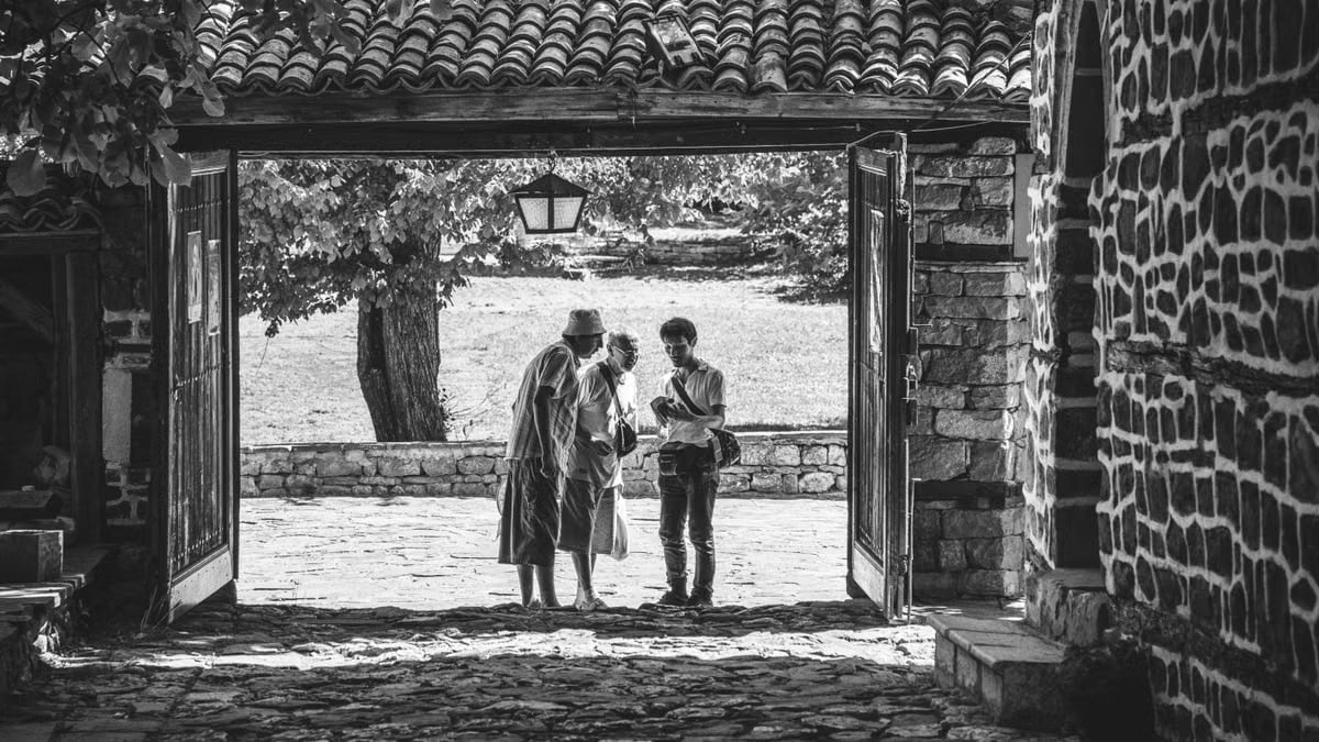 Black and white image showing three adults conversing in a serene courtyard.